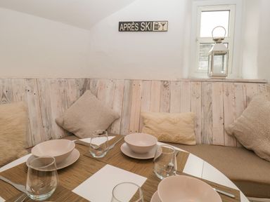 A dining area with a round white table set with bowls and glasses and cushioned bench seating with pillows at Dixon Court in Ambleside
