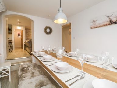 A dining room with a wooden table set with white dishes and glassware at Dixon Court in Ambleside