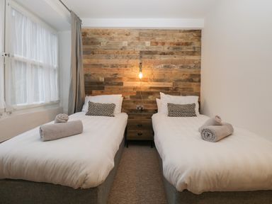 A bedroom with two single beds a wooden headboard and a window with curtains at Dixon Court in Ambleside