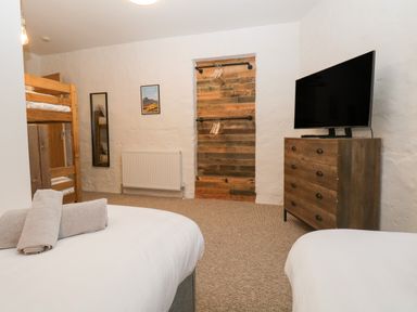 A bedroom with bunk beds a wooden dresser a wall-mounted tv and a wooden panel with hangers at Dixon Court Ambleside