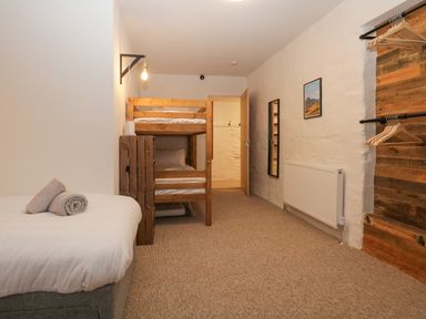 A bedroom with a single bed and bunk beds with towels on the bed a wall mirror wooden hangers on racks and a radiator at Dixon Court Ambleside