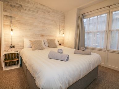 A bedroom with a large bed two pillows two rolled towels bedside shelves hanging lightbulbs and windows with curtains at Dixon Court in Ambleside