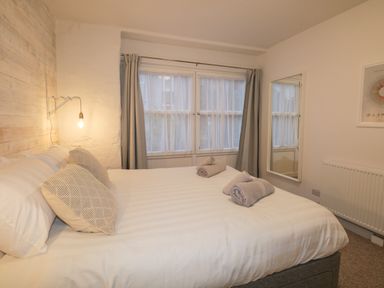A bedroom with a bed with pillows and rolled towels next to a window with curtains and a mirror on the wall at Dixon Court in Ambleside