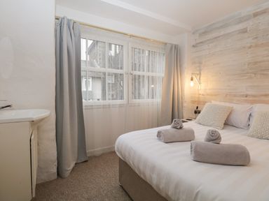 A bedroom with a bed, pillows, rolled towels, a window with curtains, a wall lamp, and a small sink at Dixon Court in Ambleside