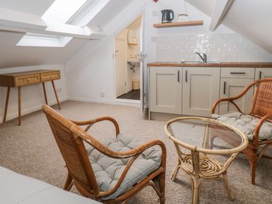A small living area with two rattan chairs and a glass coffee table near a kitchenette with sink and cabinets at Dixon Court in Ambleside