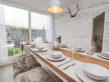 A dining table set with plates bowls and glasses in a room with wood paneled walls and a sliding glass door at Dixon Court in Ambleside