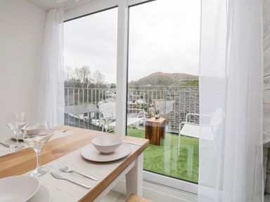 A dining table with place settings next to a glass door leading to a balcony with chairs and a small table at Dixon Court Ambleside