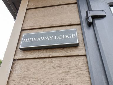 A black nameplate with white text reading Hideaway Lodge mounted on a brown wooden wall next to a black door handle at Hideaway Lodge in Runswick Bay