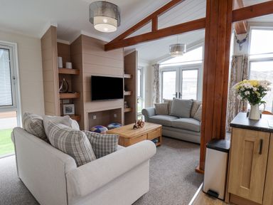 A living room with two sofas a wooden coffee table a mounted television wooden shelving and large windows at Hideaway Lodge in Runswick Bay