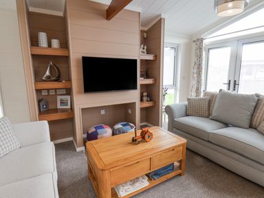 A living room with two sofas a wooden coffee table a wall-mounted TV and shelves with decorations at Hideaway Lodge in Runswick Bay