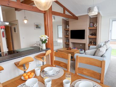 An open dining and living room area with set dining table wooden chairs and stools at Hideaway Lodge in Runswick Bay