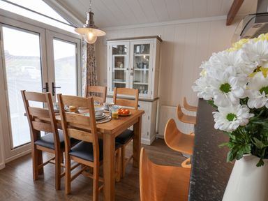 A dining area with a wooden table set for four near glass doors and a white cabinet with glass doors at Hideaway Lodge in Runswick Bay