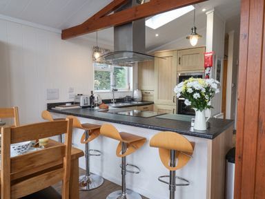 A kitchen with a black countertop bar with wooden stools and wooden cabinets at Hideaway Lodge in Runswick Bay