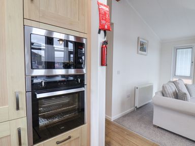 A kitchen area with built-in oven and microwave next to a living room with a sofa and a radiator at Hideaway Lodge in Runswick Bay