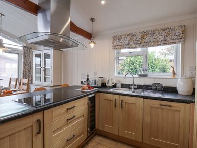 A kitchen with wooden cabinets and a black countertop with a stove sink and kettle at Hideaway Lodge in Runswick Bay