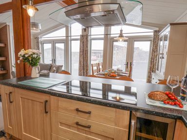 A kitchen with a black countertop and wooden cabinets with a stovetop and a dining table in the background at Hideaway Lodge in Runswick Bay