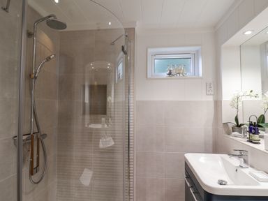 A bathroom with a shower, sink, mirror, small window, and decorative items at Hideaway Lodge in Runswick Bay