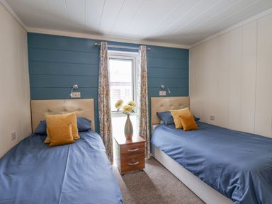 A bedroom with two single beds separated by a wooden nightstand with a vase of flowers at Hideaway Lodge in Runswick Bay