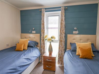 A bedroom with two single beds a window between them and a bedside table with a vase of flowers at Hideaway Lodge in Runswick Bay