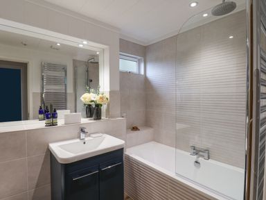 A bathroom with a sink unit, mirror, bathtub with shower screen, and flowers at Hideaway Lodge in Runswick Bay