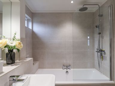 A bathroom with a bathtub shower combination and flowers in a vase on the counter at Hideaway Lodge in Runswick Bay