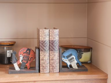 A wooden shelf with decorative guitar bookends holding two books and candles at Hideaway Lodge in Runswick Bay
