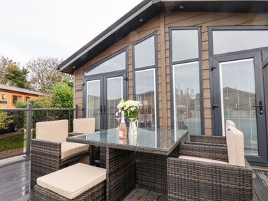 An outdoor patio area with a wicker table and chairs with beige cushions at Hideaway Lodge in Runswick Bay