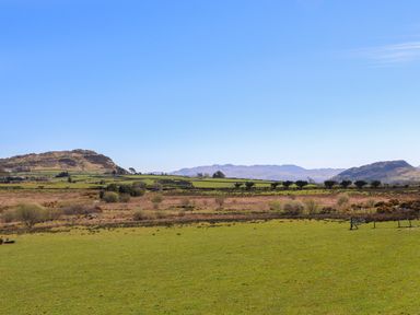 A green field with trees and hills under a clear blue sky at Hen Beudy in Porthmadog
