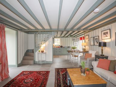 An open living and dining area with sofas rugs coffee table and stairs leading upstairs at Hen Beudy in Porthmadog