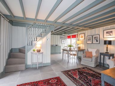 A living room and dining area with stairs table chairs armchairs and framed pictures at Hen Beudy in Porthmadog