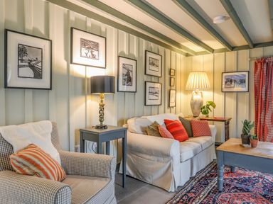 A living room with a checkered armchair and a sofa with cushions a coffee table and framed pictures on walls at Hen Beudy in Porthmadog