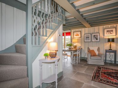 A stairway next to a small table with a lamp and plant a dining area with chairs and a table and a living area with an armchair side table and lamps at Hen Beudy in Porthmadog