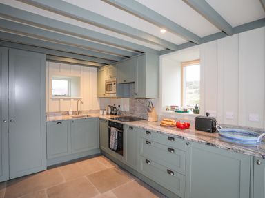 A kitchen with green cabinets granite countertops a sink an oven a microwave a toaster and windows at Hen Beudy in Porthmadog