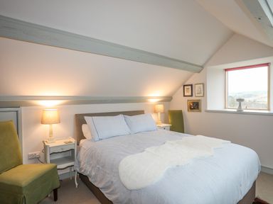 A bedroom with a double bed lamps on bedside tables green chairs and a window at Hen Beudy in Porthmadog