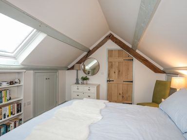 A bedroom with a bed a wooden door a dresser a round mirror a bookshelf and a skylight at Hen Beudy in Porthmadog