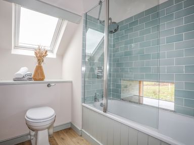 A bathroom with a toilet and a bathtub with blue tiled walls and a skylight window at Hen Beudy in Porthmadog