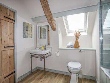 A bathroom with a wooden door a corner sink toilet towels and a vase on a shelf under a skylight at Hen Beudy in Porthmadog