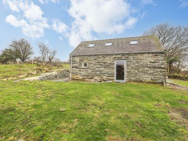 A stone building with skylights and a glass door on a grassy plot with trees and a fence at Hen Beudy in Porthmadog