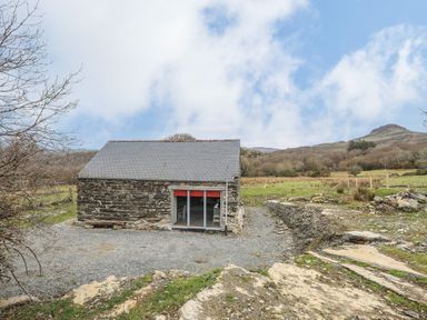 A stone building with a slate roof and glass sliding doors in a rural landscape at Hen Beudy in Porthmadog