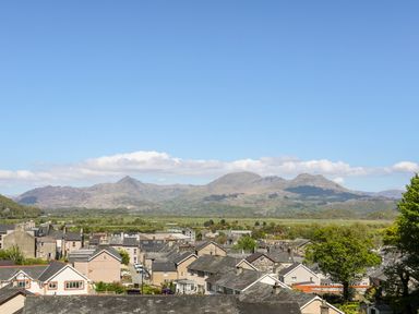 A town with houses and trees with mountains and blue sky in the background at Hen Beudy in Porthmadog
