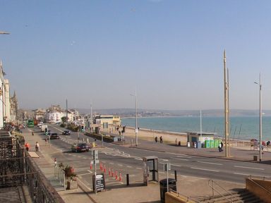 A coastal road with vehicles and pedestrians next to a beach and sea at Sunrise Apartment in Weymouth