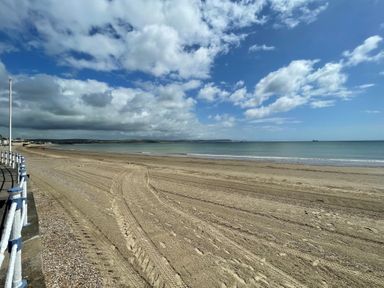A sandy beach with tire tracks and footprints next to a sea and cloudy sky at Sunrise Apartment in Weymouth