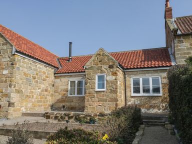 A stone cottage with red tile roof and white framed windows surrounded by a garden path and shrubs at Rose Cottage in Faceby near Swainby