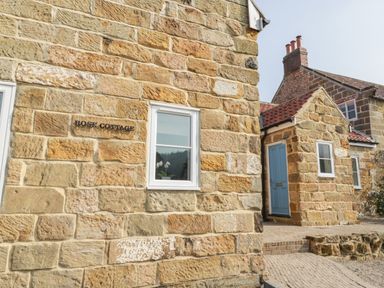 An exterior view of a stone cottage with a blue door and a small window with a plant inside at Rose Cottage Faceby near Swainby