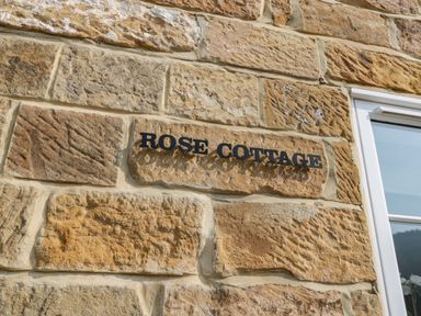 A stone wall with a sign that reads Rose Cottage next to a window at Rose Cottage Faceby near Swainby