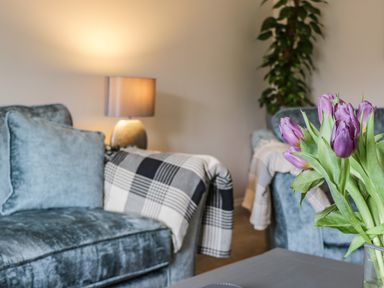 A living room with purple flowers on a table blue sofas a lamp and a plant at Rose Cottage Faceby near Swainby