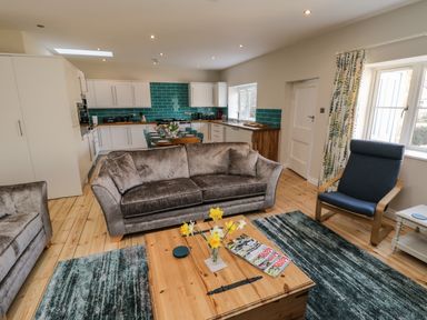 An open living room and kitchen with gray sofas a wooden coffee table and a blue armchair at Rose Cottage in Faceby near Swainby