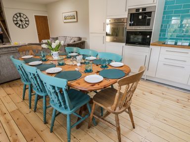 Kitchen and dining area with wooden table set for eight and teal and wooden chairs at Rose Cottage in Faceby near Swainby