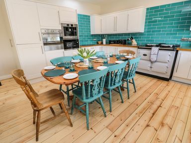 A kitchen with a wooden dining table set with plates and glasses surrounded by blue and wooden chairs at Rose Cottage Faceby near Swainby