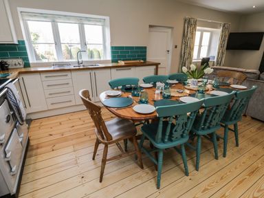 A kitchen with a wooden dining table set with plates glasses and flowers and teal chairs at Rose Cottage in Faceby near Swainby